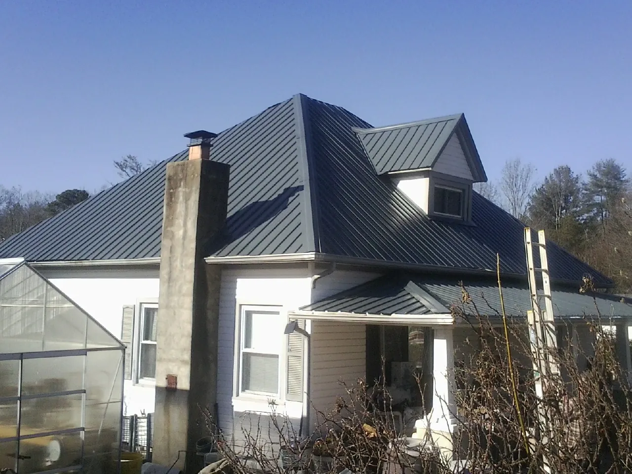 Dark blue standing seam metal roof on a white farmhouse with dormer — Slate & Tile Roof Repair by Roofing Brothers in Marsteller