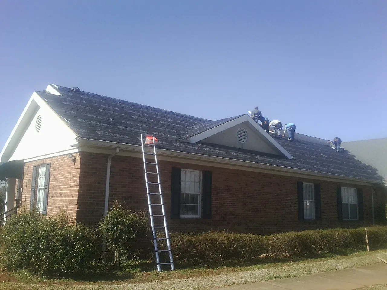 Crew tearing shingles off a brick ranch roof with a ladder set — Emergency Roof Repair work by our crew in Marsteller