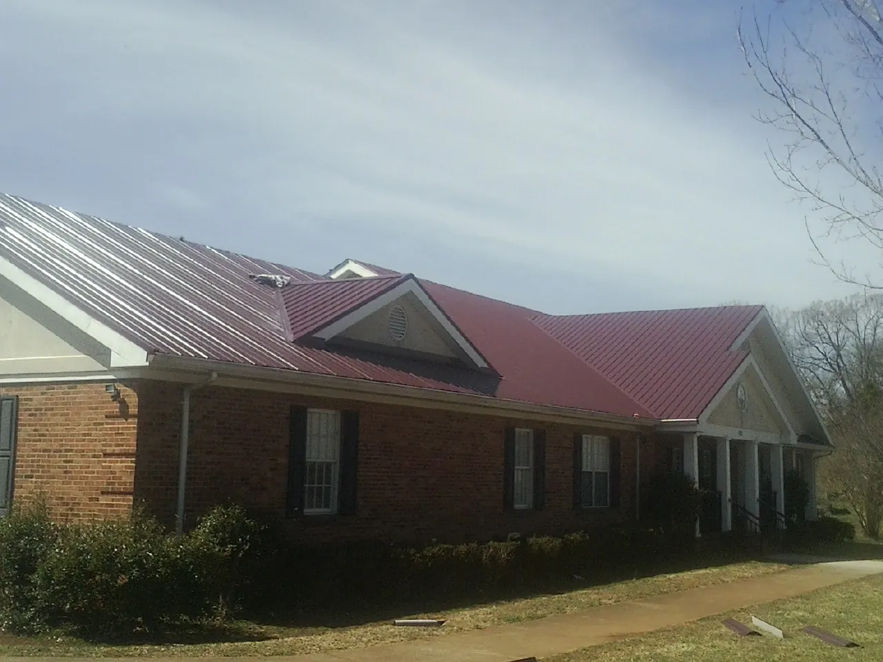 Red metal roof with gabled entries on a long brick building, from a Hail Damage Roof Repair job in Marsteller