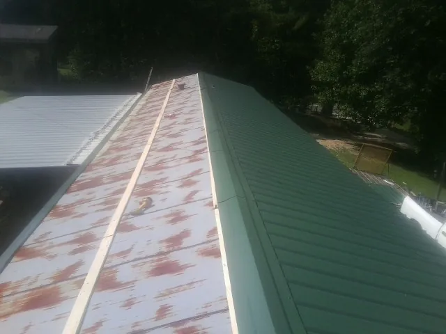 Old rusted panels beside newly installed green metal roofing — Wind Damage Roof Repair by Roofing Brothers in Marsteller