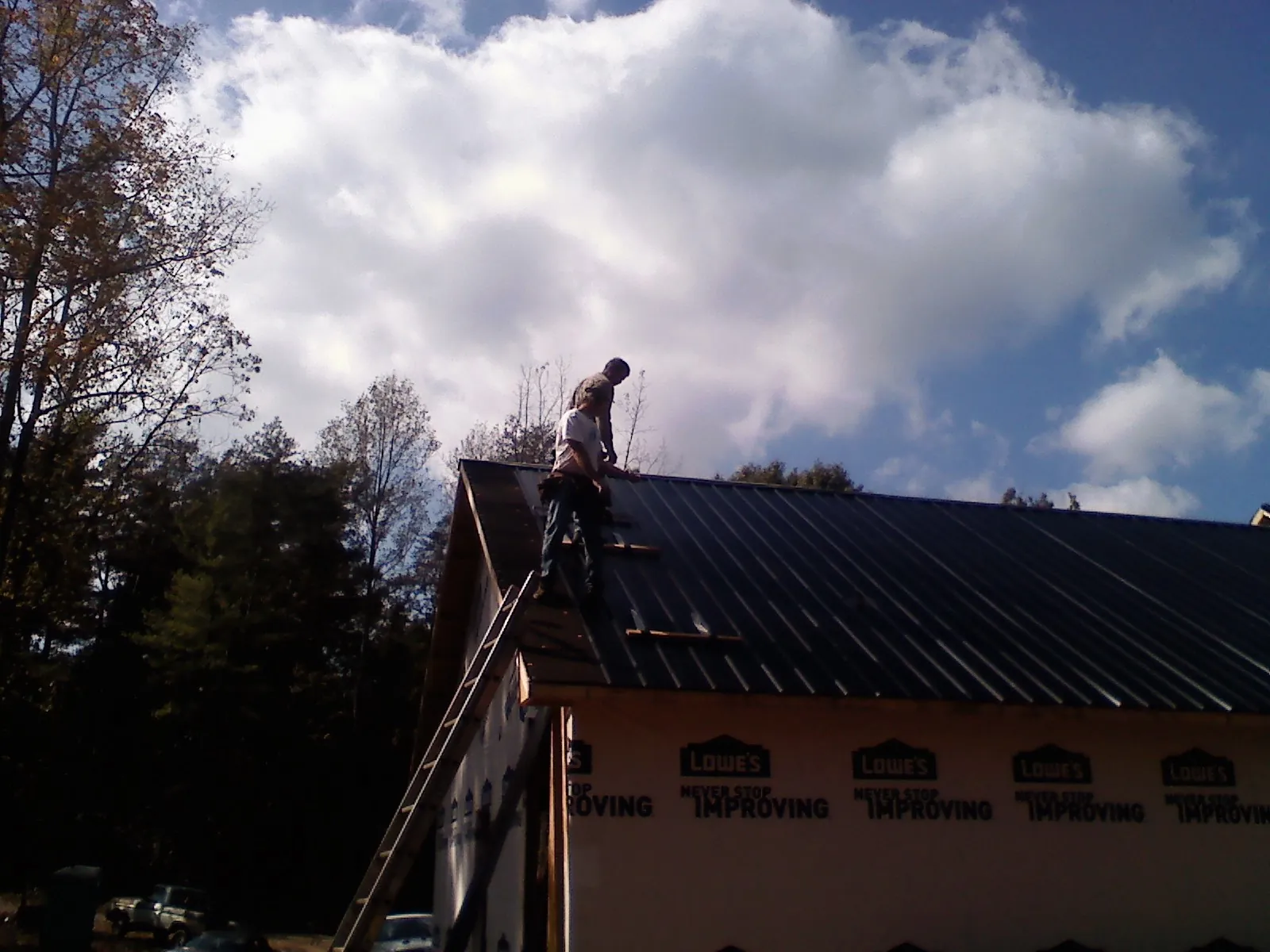 Roofer fastening dark metal panels high against a cloudy sky, from a Roof Inspection job in Marsteller