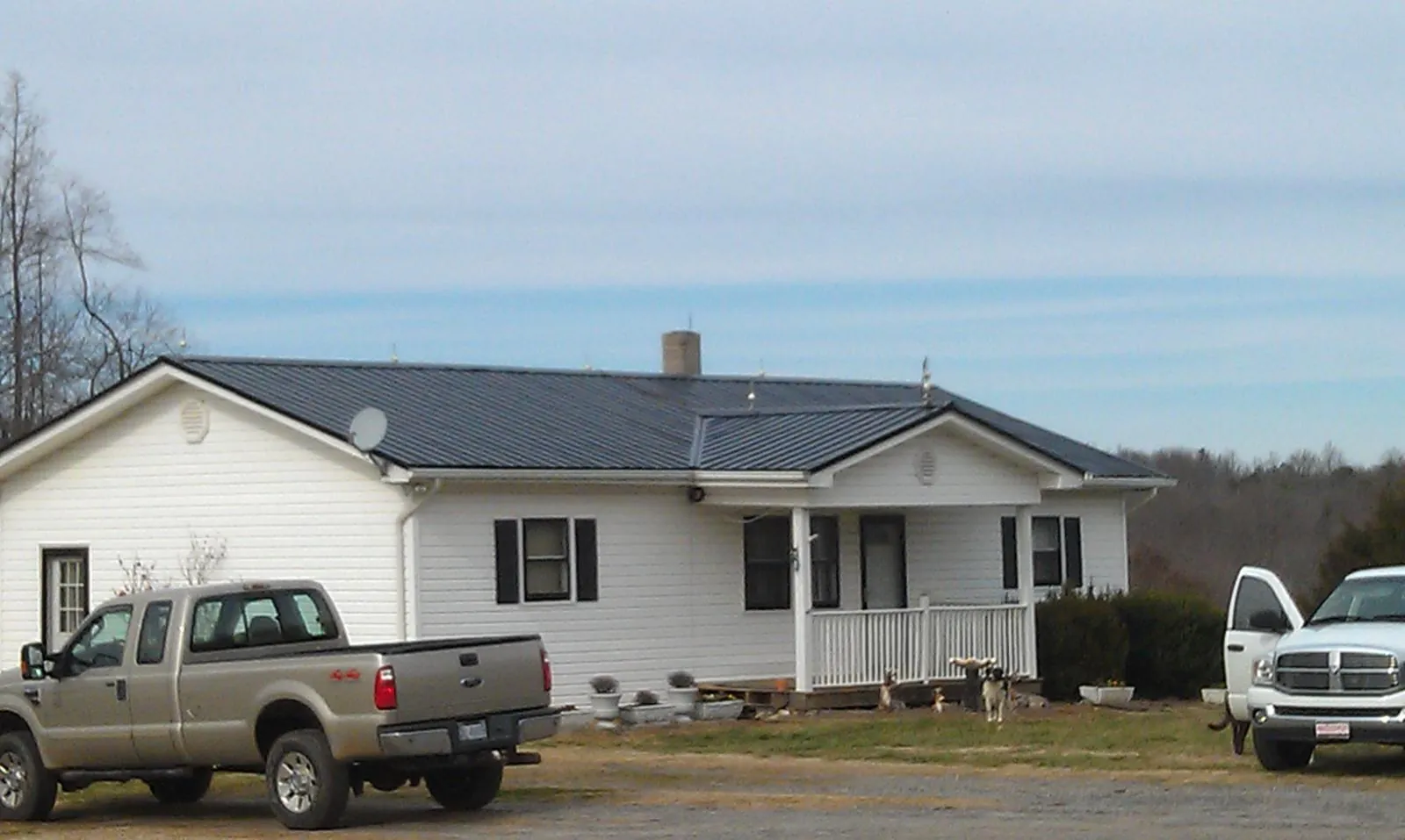 Finished dark metal roof on a white ranch home with work trucks parked in Marsteller