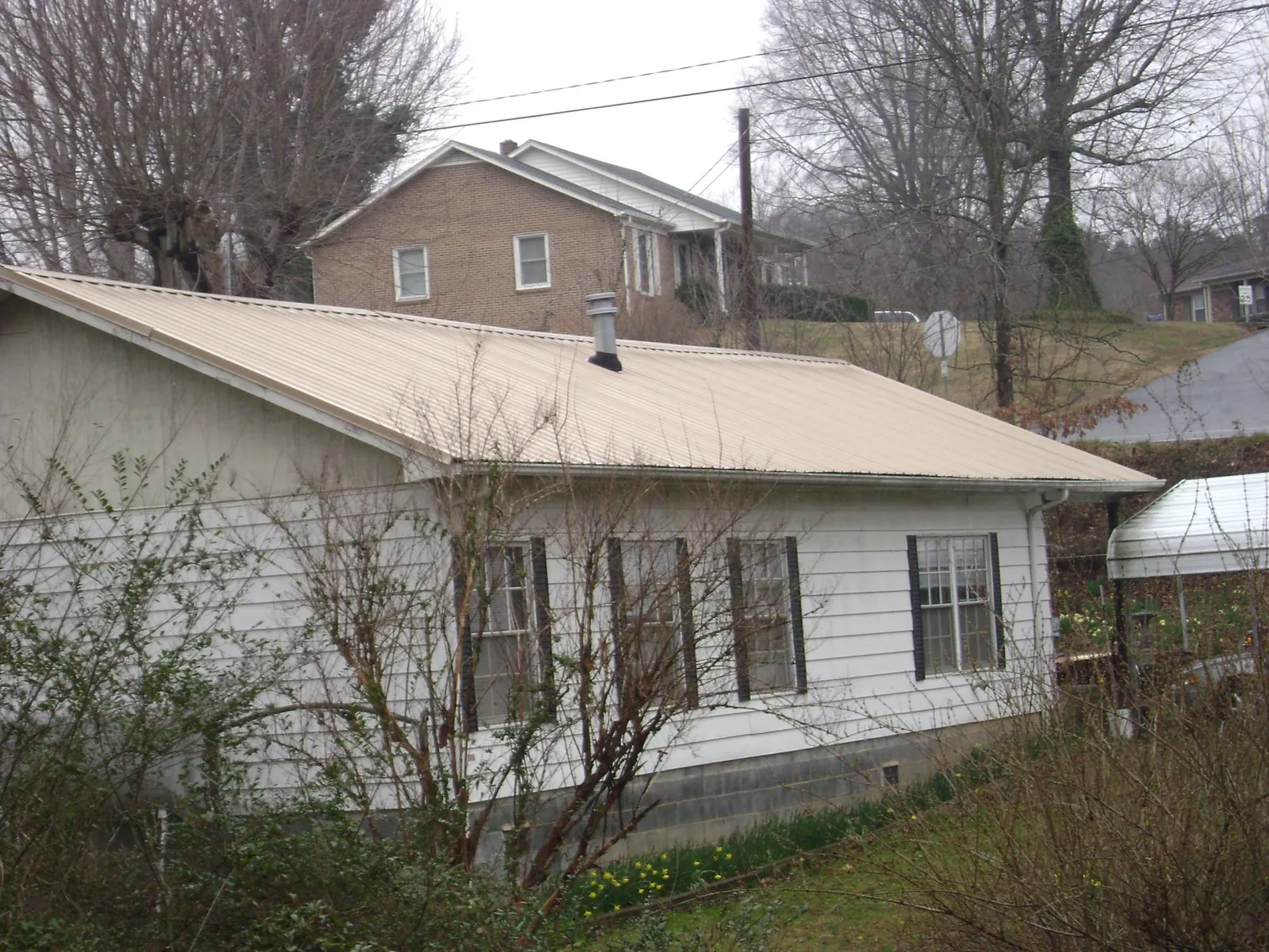 Tan metal roof on a white sided house set into a hillside — Commercial Roofing by Roofing Brothers in Marsteller